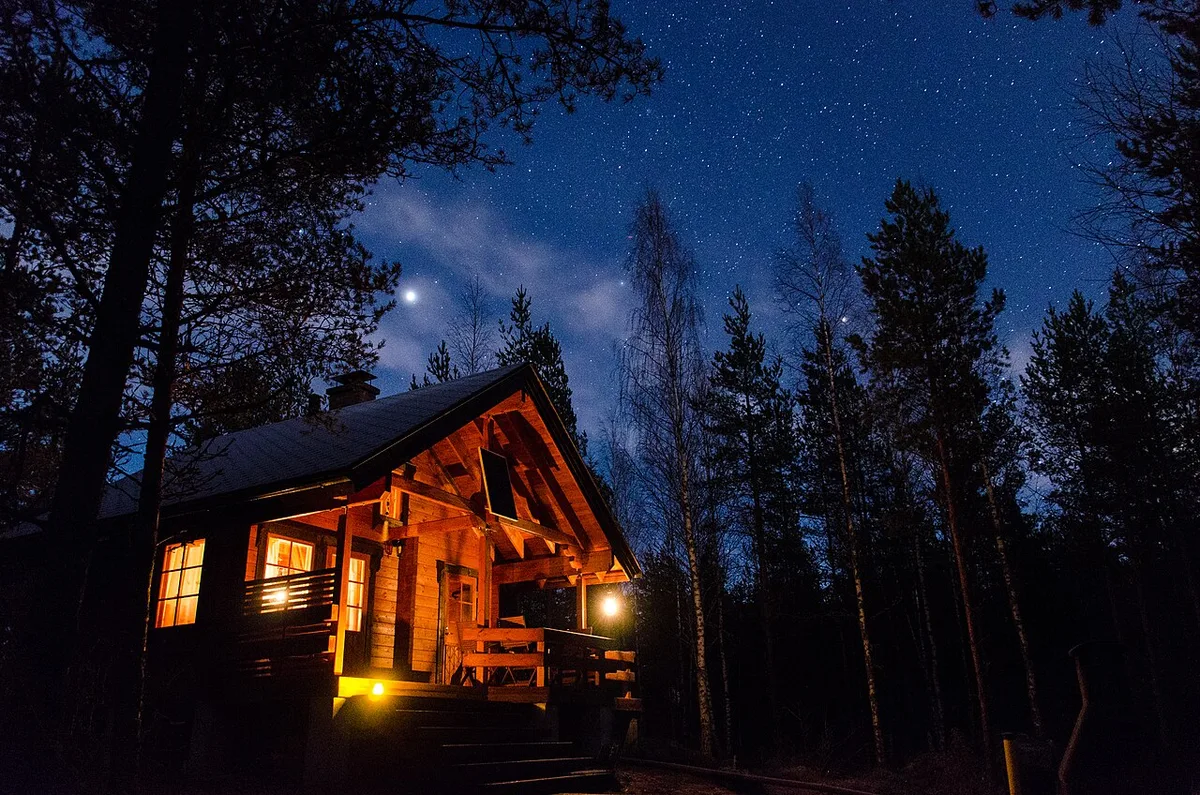 Valaistu hirsimökki tähtitaivaan alla
