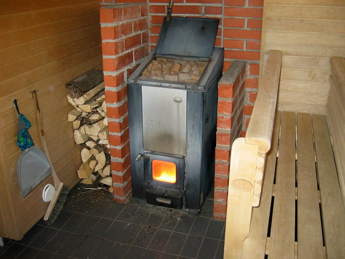 Puulämmitteinen kiuas saunassa, vieressä halkoja