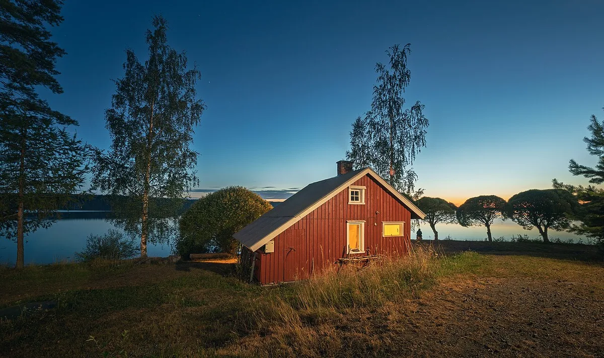 Punainen saunarakennus järven rannalla iltavalossa
